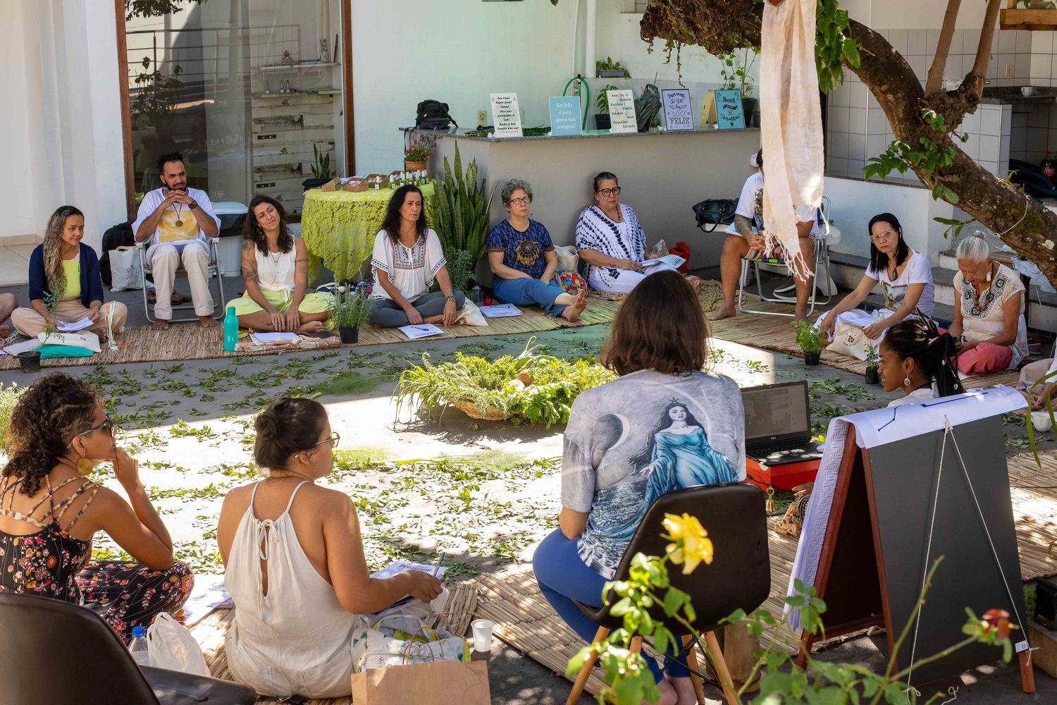 Roda de vivência: pessoas sentadas em círculo no pátio da Casa Saberes de Raízes, entre plantas e um cavalete